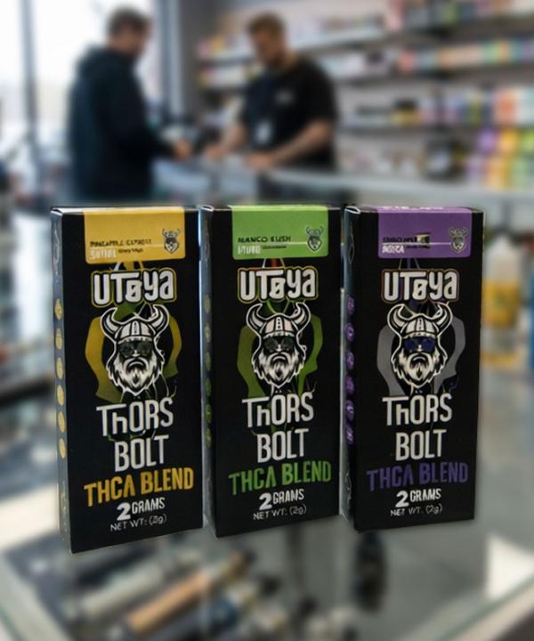 Three varieties of Utoya Thor's Bolt 2 gram THCA disposable vape boxes—Sativa, Hybrid, and Indica—displayed on a glass counter in a smoke shop.